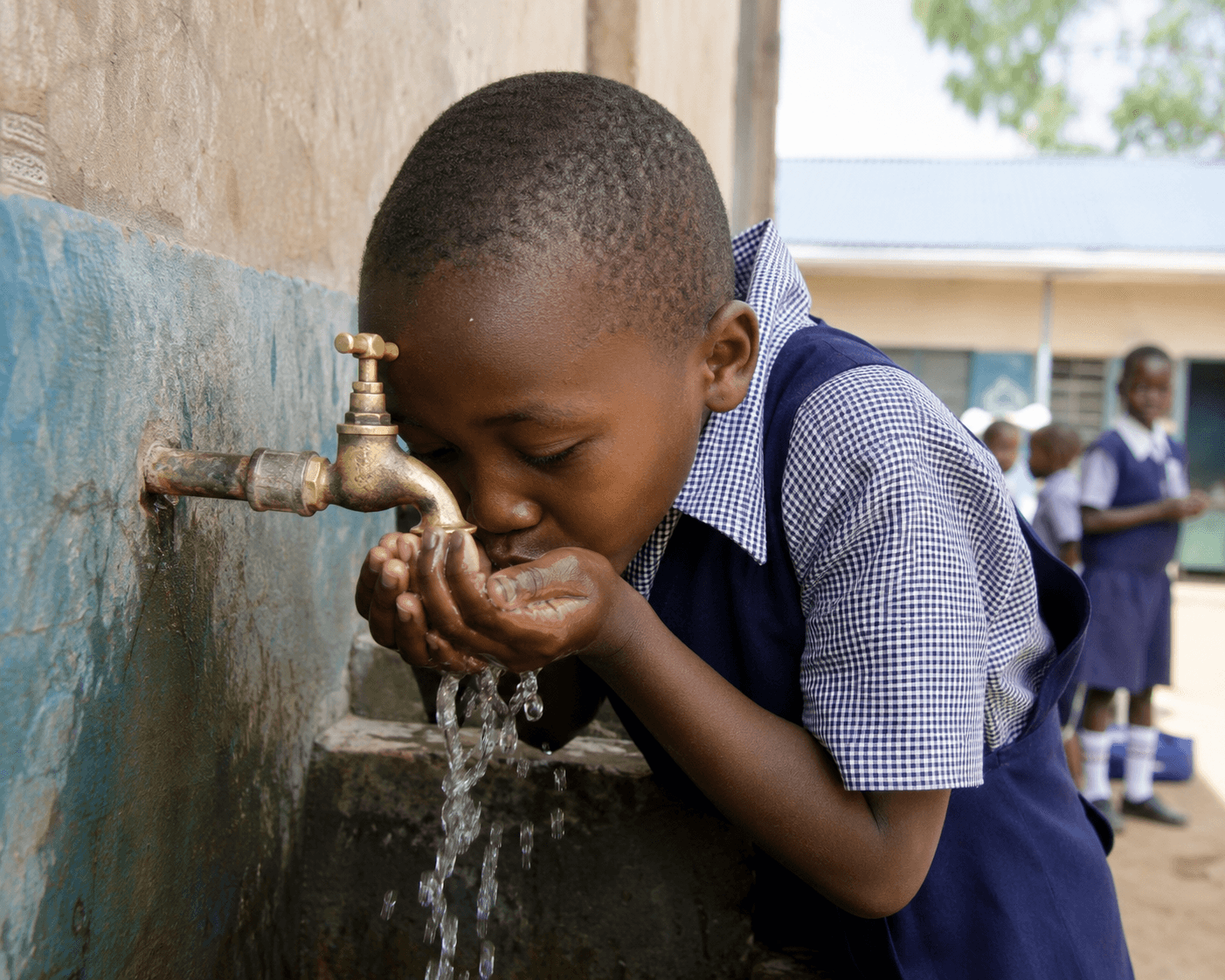 Kenyan schoolchild drinking clean water from an outdoor tap at school